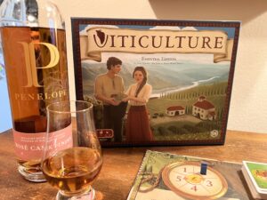 A bottle of Penelope Rosé Cask Finish next to the board game Viticulture Essential Edition.